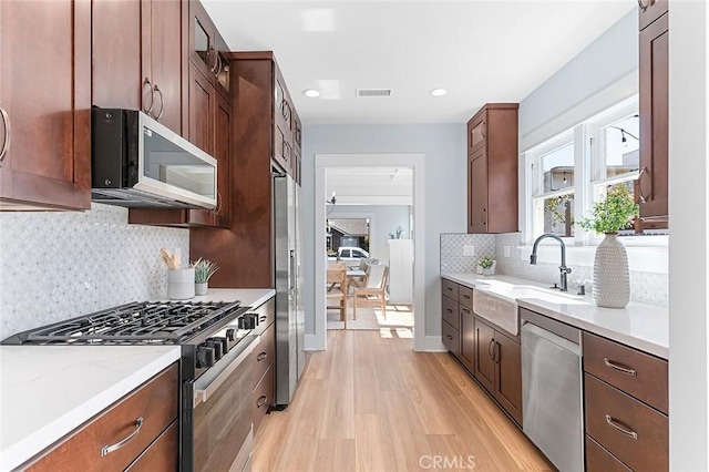 kitchen featuring stainless steel appliances, visible vents, glass insert cabinets, a sink, and light wood-type flooring