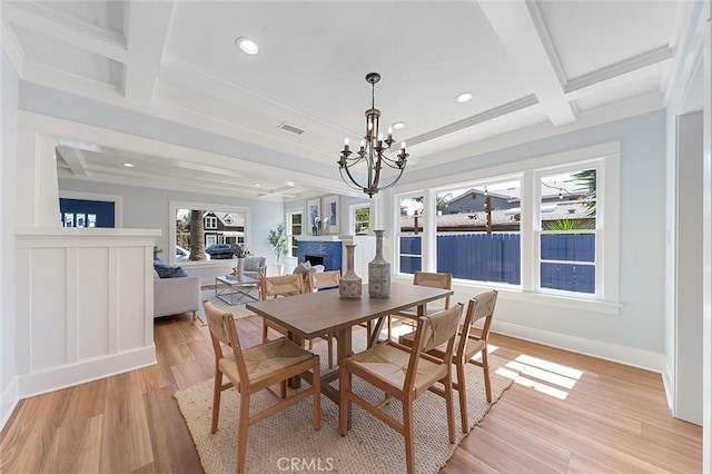 dining room with visible vents, coffered ceiling, light wood-type flooring, a fireplace, and beam ceiling