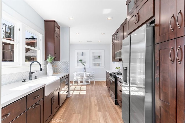 kitchen featuring stainless steel appliances, a sink, dark brown cabinets, light wood finished floors, and tasteful backsplash