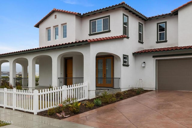 mediterranean / spanish house featuring an attached garage, fence, concrete driveway, french doors, and stucco siding