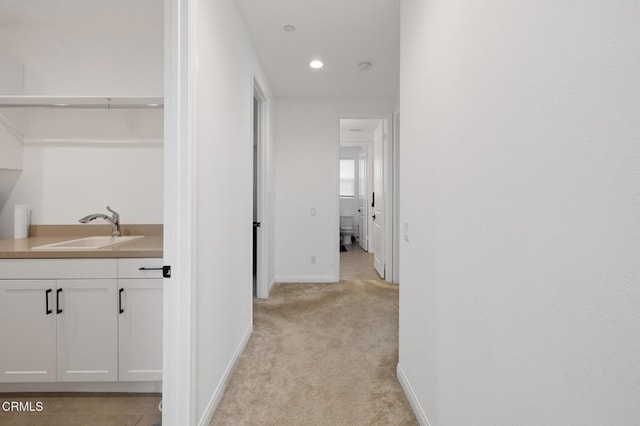 hallway featuring baseboards, recessed lighting, a sink, and light colored carpet