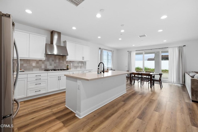 kitchen featuring visible vents, light wood-style floors, light countertops, freestanding refrigerator, and wall chimney exhaust hood