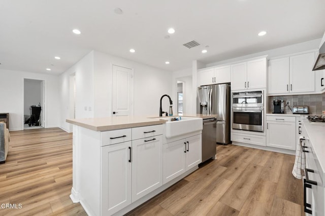 kitchen with light wood finished floors, a center island with sink, visible vents, and stainless steel appliances