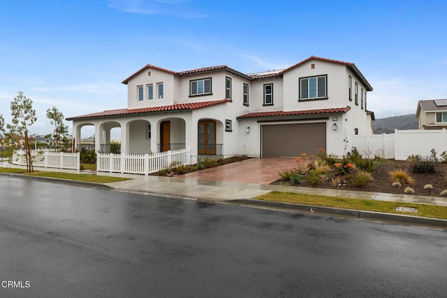 mediterranean / spanish home featuring driveway, an attached garage, covered porch, fence, and stucco siding