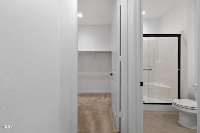 full bathroom with baseboards, toilet, tile patterned floors, a spacious closet, and a shower stall