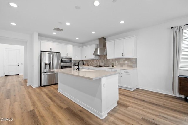 kitchen with stainless steel appliances, tasteful backsplash, light countertops, a sink, and wall chimney range hood