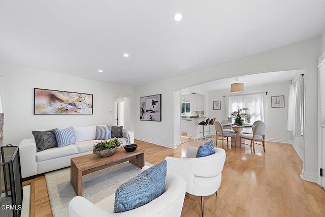 living area with arched walkways, recessed lighting, light wood-style flooring, and baseboards