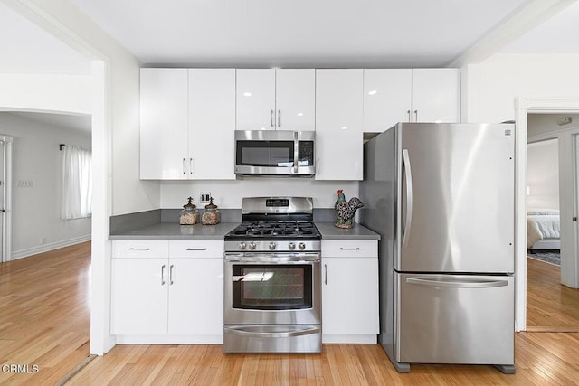 kitchen with dark countertops, light wood finished floors, appliances with stainless steel finishes, and white cabinets