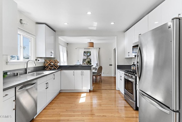 kitchen with appliances with stainless steel finishes, dark countertops, light wood-style floors, and a sink