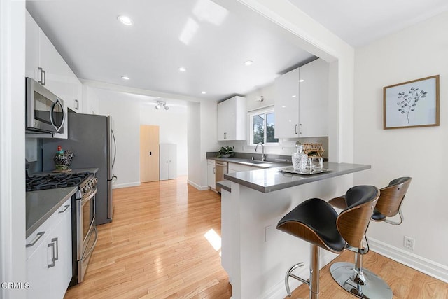 kitchen featuring dark countertops, appliances with stainless steel finishes, a sink, a peninsula, and a kitchen bar