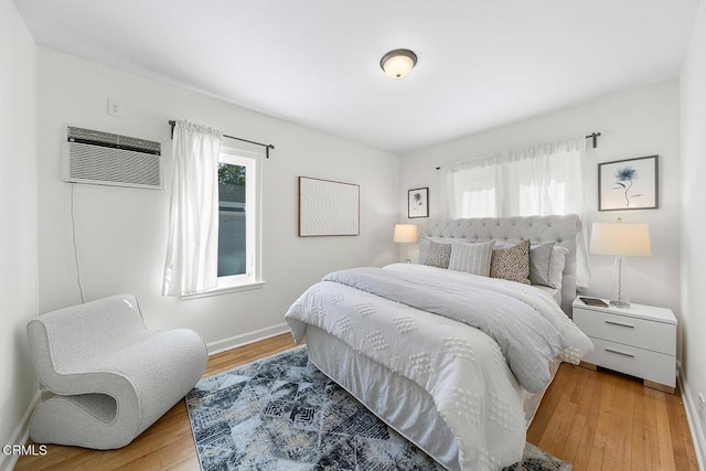 bedroom with baseboards, a wall mounted AC, and light wood-style floors