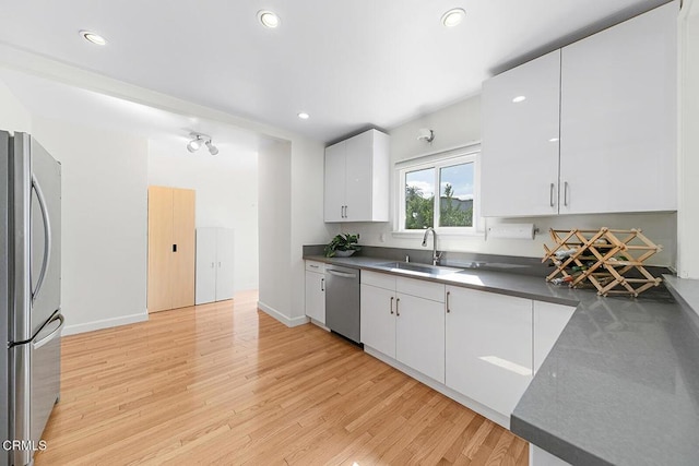 kitchen featuring white cabinets, dark countertops, appliances with stainless steel finishes, light wood-style floors, and a sink