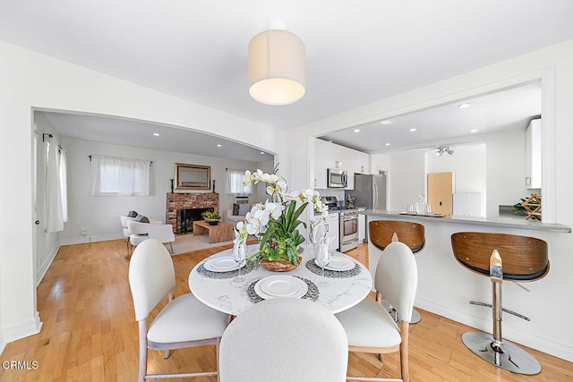 dining area featuring light wood-type flooring, a fireplace, baseboards, and recessed lighting