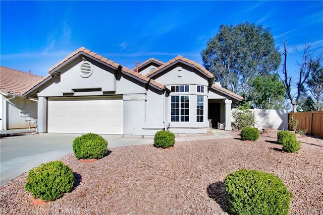 view of front of house featuring stucco siding, concrete driveway, an attached garage, fence, and a tiled roof