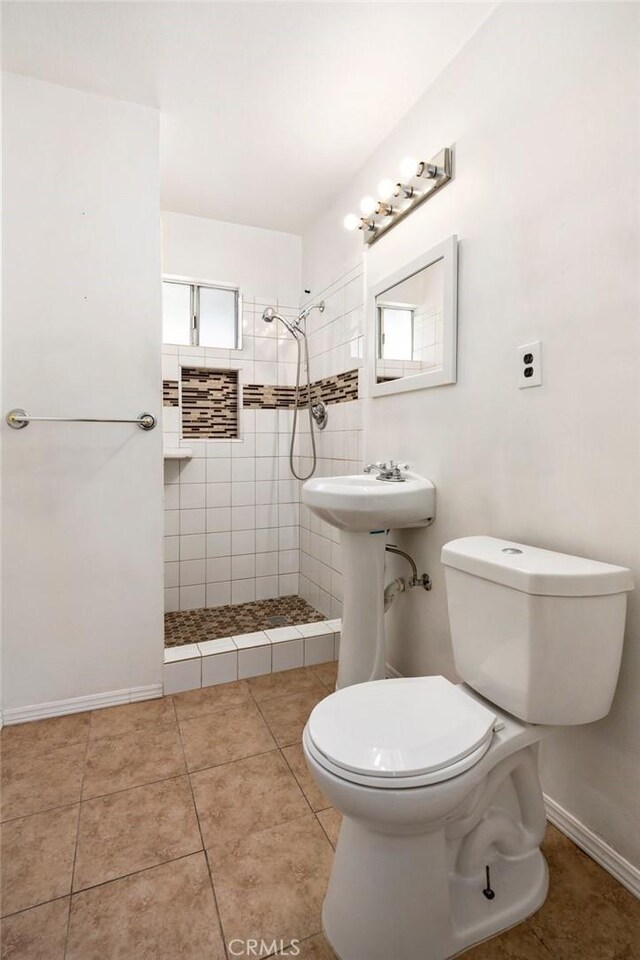 full bath featuring tile patterned floors, a tile shower, toilet, and baseboards