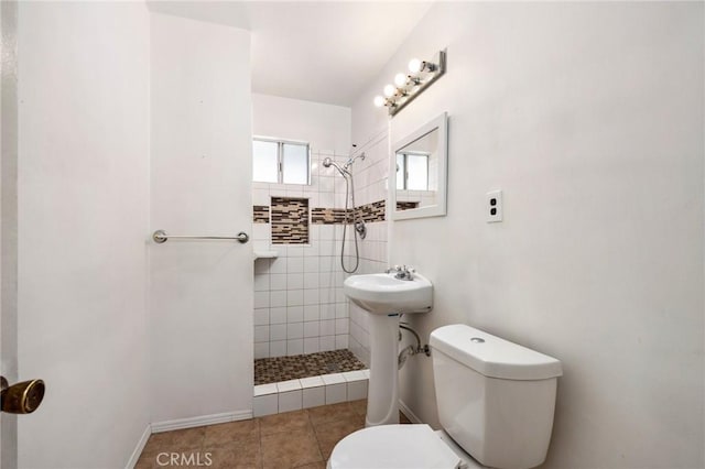 bathroom with a sink, a tile shower, toilet, and tile patterned floors