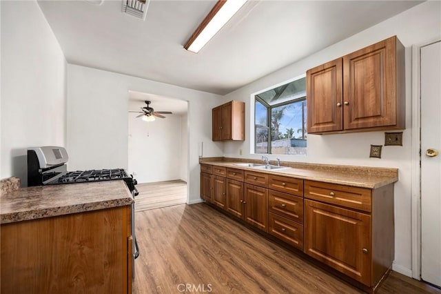 kitchen featuring dark wood finished floors, stainless steel gas range oven, a sink, and visible vents