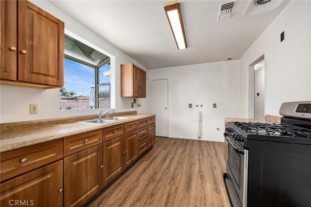 kitchen with stainless steel range with gas cooktop, visible vents, brown cabinetry, and a sink