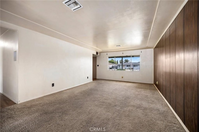 unfurnished room with carpet, wooden walls, visible vents, and baseboards