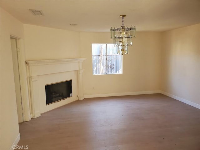 unfurnished living room with wood finished floors, visible vents, baseboards, a glass covered fireplace, and an inviting chandelier