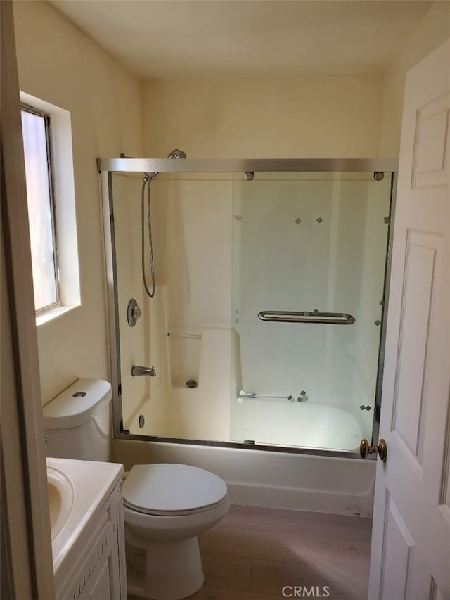 bathroom with toilet, enclosed tub / shower combo, wood finished floors, and vanity