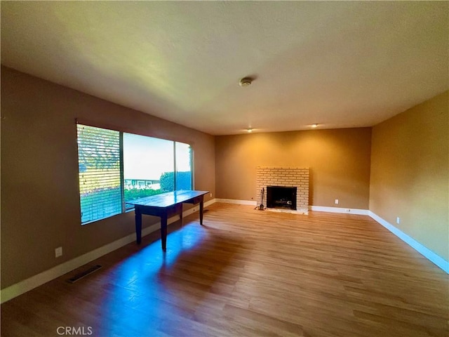 unfurnished living room with a brick fireplace, wood finished floors, visible vents, and baseboards