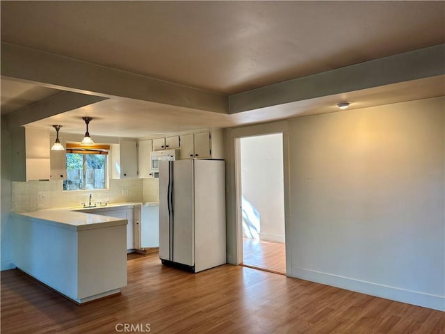 kitchen featuring white appliances, light countertops, a peninsula, and dark wood-style flooring