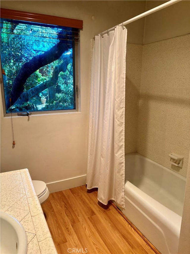 bathroom with toilet, shower / tub combo, a sink, wood finished floors, and baseboards