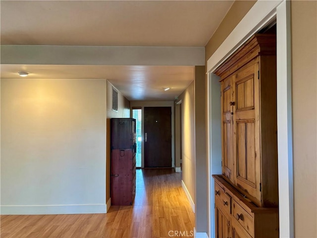 corridor with light wood-type flooring, visible vents, and baseboards