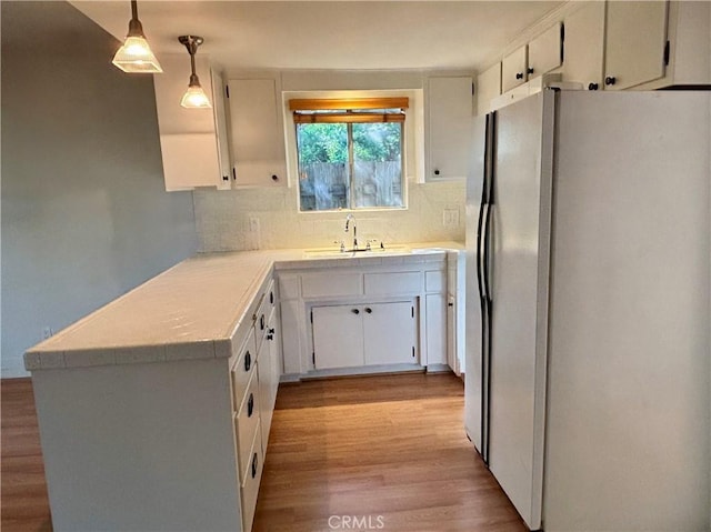 kitchen with light wood finished floors, light countertops, decorative backsplash, freestanding refrigerator, and a sink