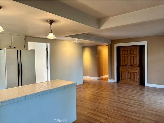 kitchen with baseboards, tile countertops, wood finished floors, freestanding refrigerator, and white cabinetry