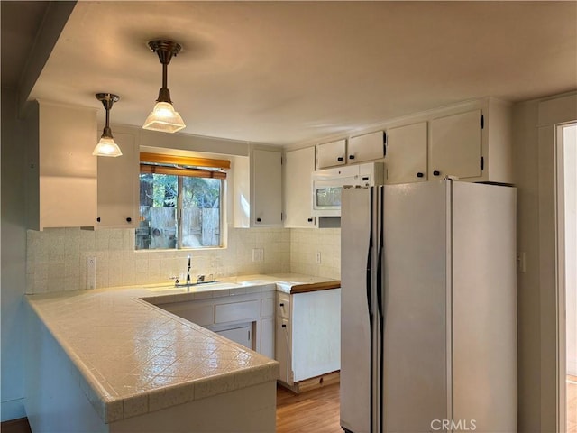 kitchen featuring backsplash, white microwave, freestanding refrigerator, white cabinets, and a sink