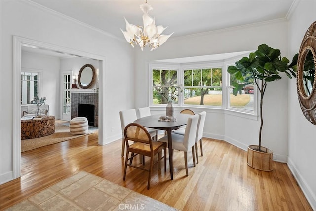 dining room with a notable chandelier, crown molding, light wood-style flooring, a tiled fireplace, and baseboards