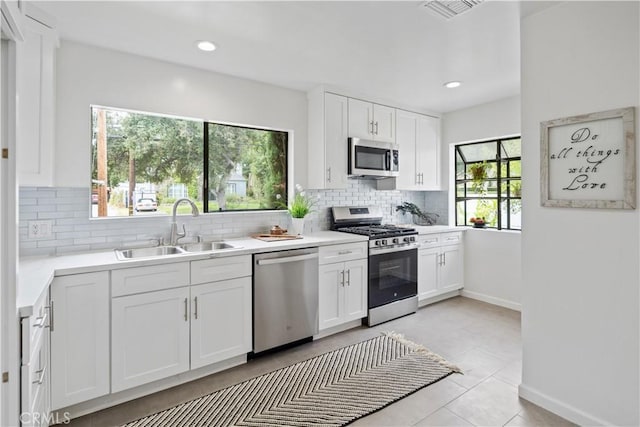 kitchen featuring backsplash, appliances with stainless steel finishes, white cabinets, and a sink