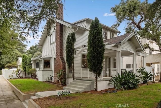 view of front of home with covered porch, a chimney, a front yard, and fence