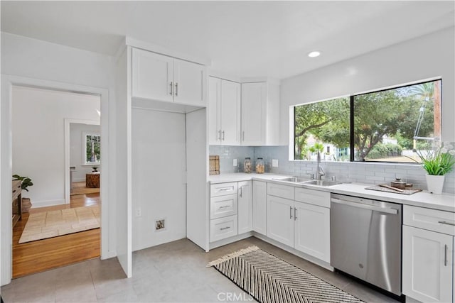 kitchen featuring stainless steel dishwasher, backsplash, a sink, and white cabinetry