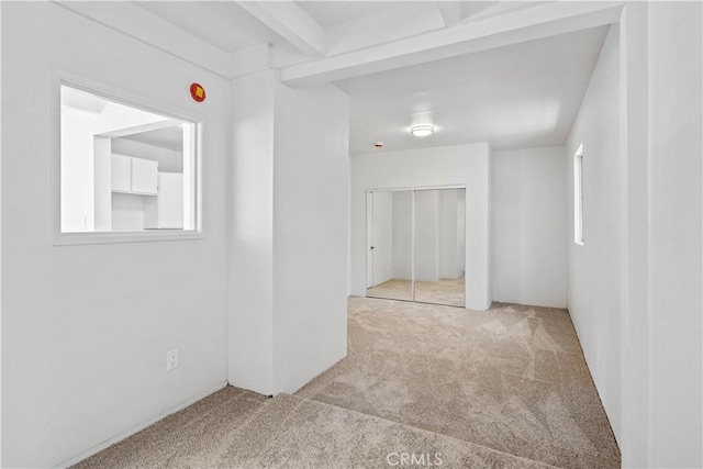 carpeted spare room featuring a healthy amount of sunlight and beamed ceiling