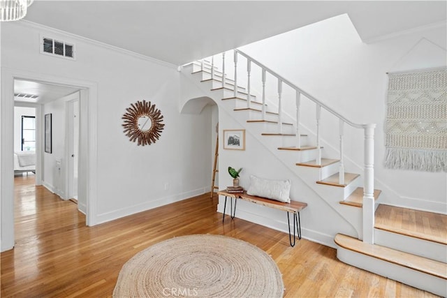 staircase with arched walkways, wood finished floors, visible vents, and crown molding