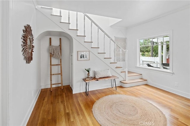 staircase with ornamental molding, wood finished floors, and baseboards