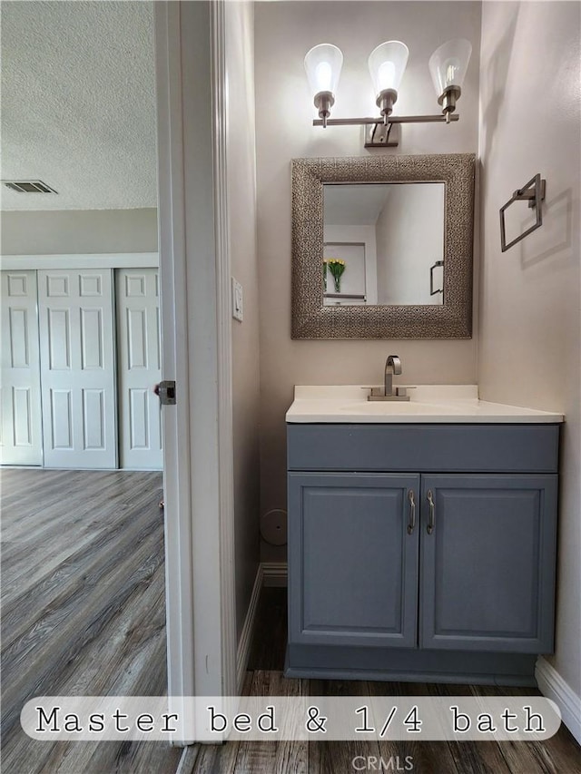 bathroom featuring baseboards, visible vents, wood finished floors, a textured ceiling, and vanity