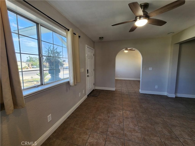 spare room with arched walkways, tile patterned flooring, a ceiling fan, and baseboards