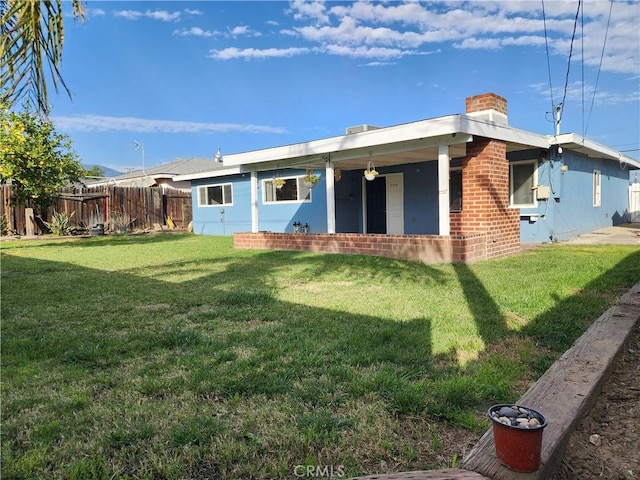 back of property with a chimney, fence, a lawn, and brick siding