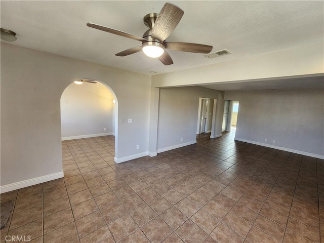 tiled empty room with arched walkways, a ceiling fan, visible vents, and baseboards