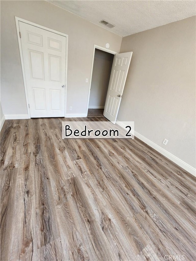 unfurnished bedroom with baseboards, a textured ceiling, visible vents, and wood finished floors