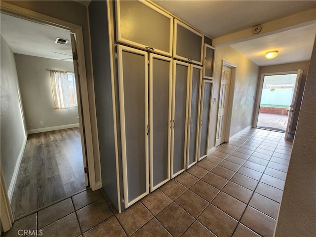 hallway with dark tile patterned flooring, a wealth of natural light, visible vents, and baseboards