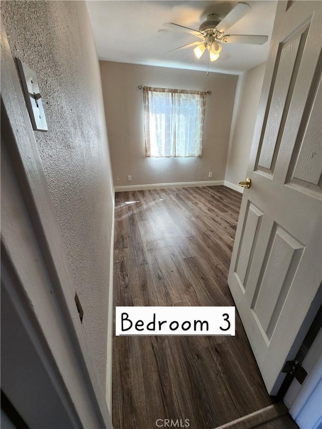 spare room with ceiling fan, baseboards, wood finished floors, and a textured wall