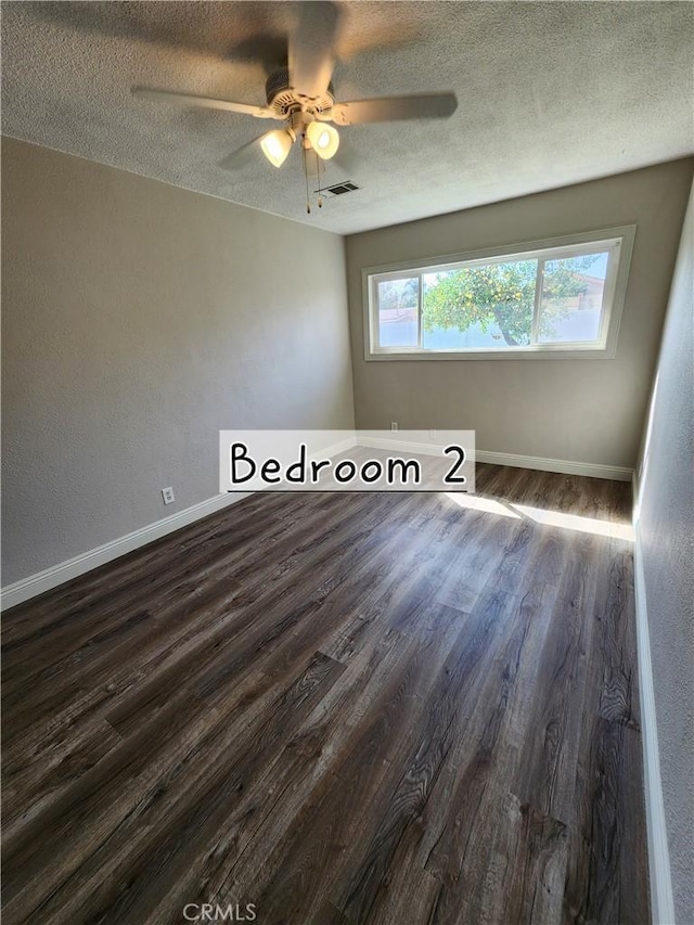 unfurnished room featuring baseboards, visible vents, dark wood finished floors, and a textured ceiling