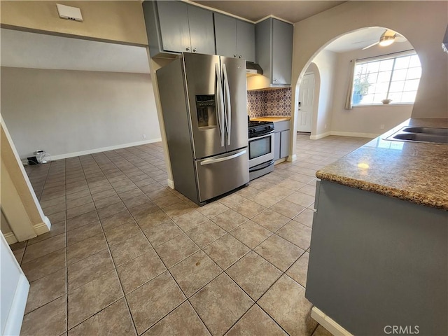 kitchen featuring arched walkways, range hood, tasteful backsplash, gray cabinets, and appliances with stainless steel finishes