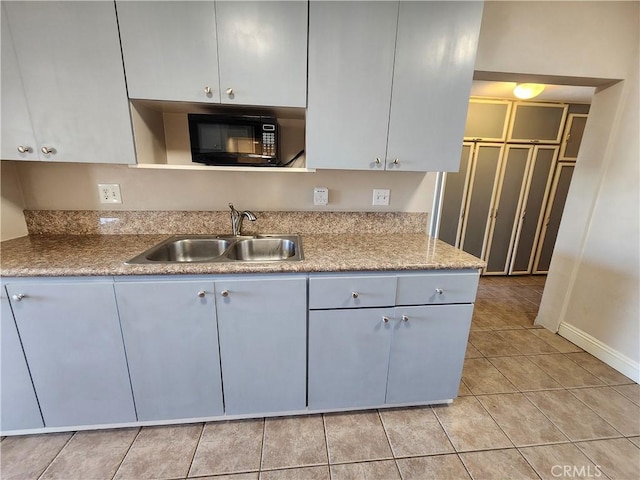 kitchen with black microwave, white cabinets, a sink, and light tile patterned flooring