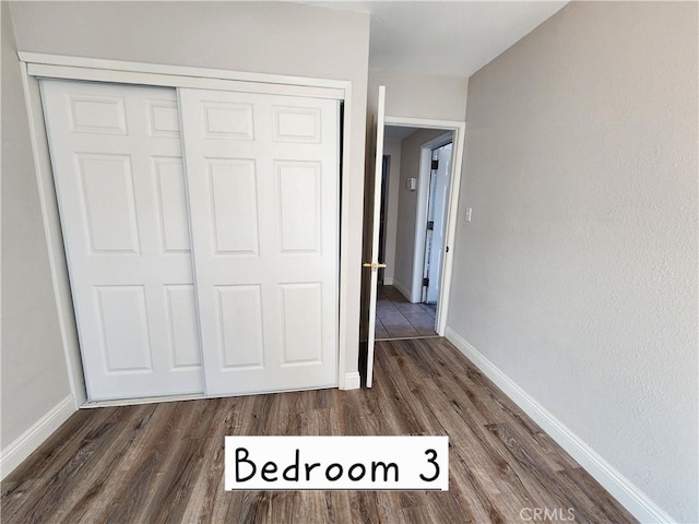 unfurnished bedroom with a closet, dark wood finished floors, and baseboards